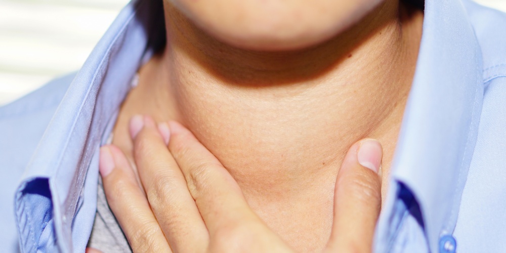 En person håller handen mot sin hals, klädd i blå skjorta, vilket kan tyda på halsont.