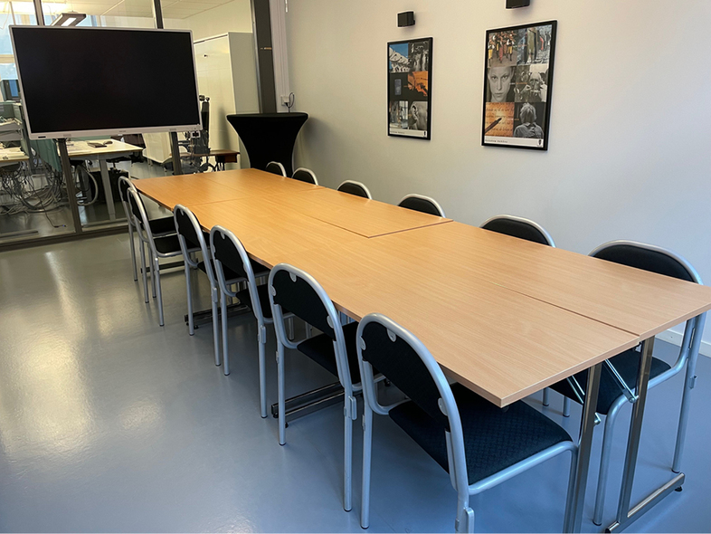 Ett modernt konferensrum med långbord, svarta stolar, stor skärm och två tavlor på väggen.