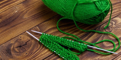 Grönt garnnystan och stickning på träbord med två stickor och påbörjat arbete.