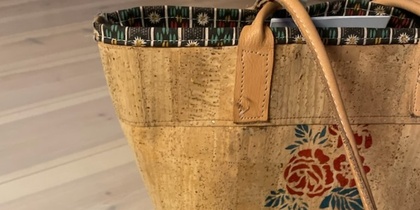 Två väskor i korkmaterial med blommönster, en större handväska och en mindre necessär, står på ett ljust trägolv.