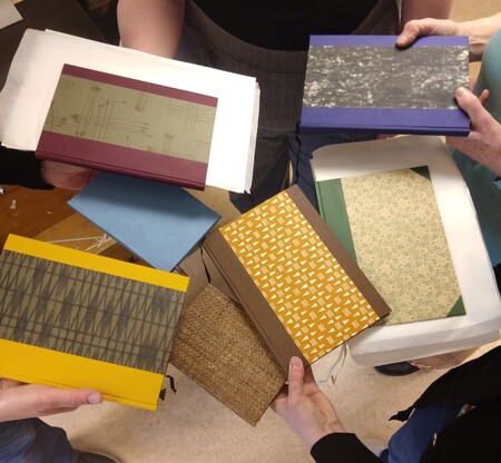 Flera personer håller upp handgjorda böcker med färgglada och mönstrade omslag i en cirkel.