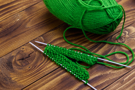 Grönt garnnystan och stickning på träbord med två stickor och påbörjat arbete.