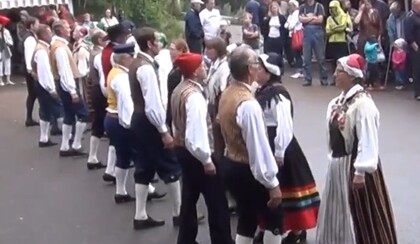 En grupp människor i traditionella folkdräkter dansar utomhus inför en publik.
