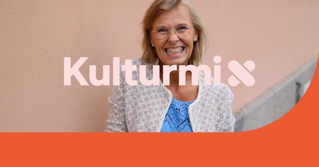 Leende kvinna med glasögon står mot en ljus vägg, texten 'Kulturmix' syns över bilden.
