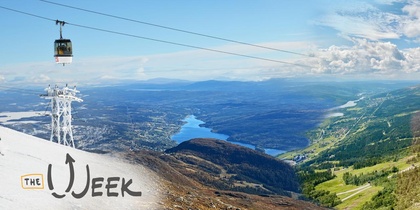 Landskapsvy med linbana över snötäckta och gröna berg, sjö och blå himmel.