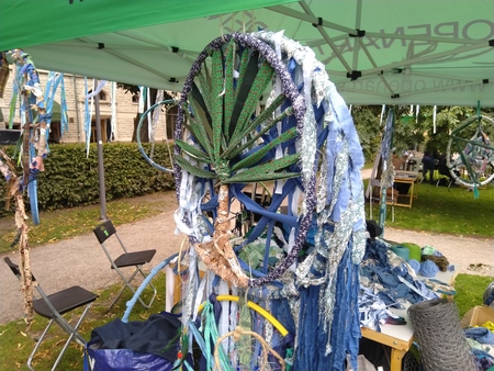 Stort hjul dekorerat med blå och gröna tygremsor under ett tält på en utomhusmarknad.