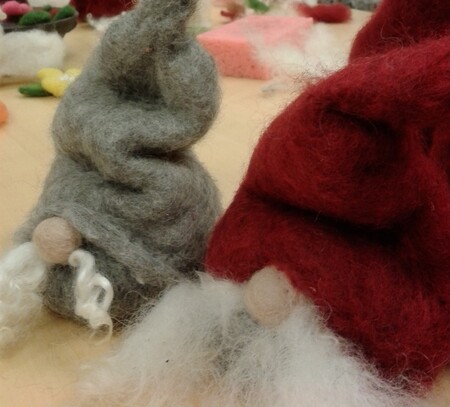 Två tovade tomtar i grått och rött med stora näsor och vita skägg står på ett bord.