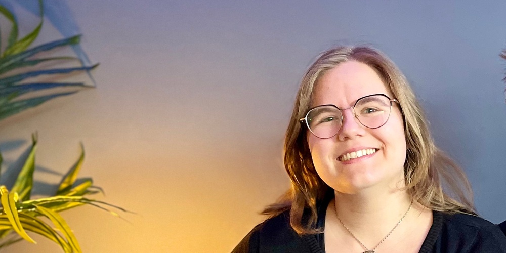 Två leende personer sitter tillsammans i en blå soffa i ett rum med blå vägg och grön växt.