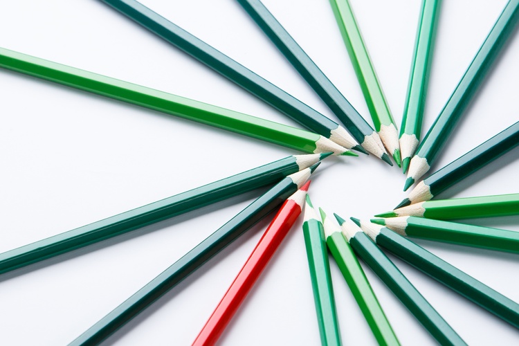 Flera gröna och en röd färgpenna ligger i en cirkel på ett vitt underlag.