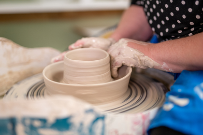En person formar lera på en drejskiva, händerna täckta av lera, fokus på keramikskålen som skapas.