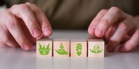 Två händer placerar träklossar med gröna miljöikoner på ett bord.