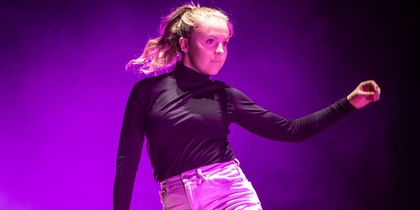 En person dansar barfota på en scen med lila ljus och rökeffekter.