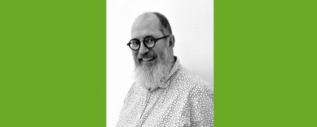 Man med glasögon och skägg ler mot kameran, svartvit bild med grön bakgrund.