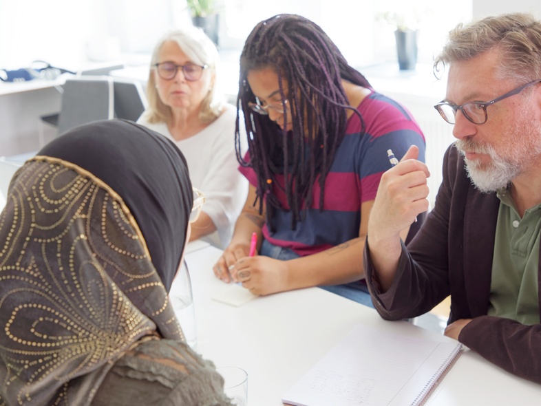 Fem personer sitter runt ett bord och diskuterar i ett ljust kontorsrum.