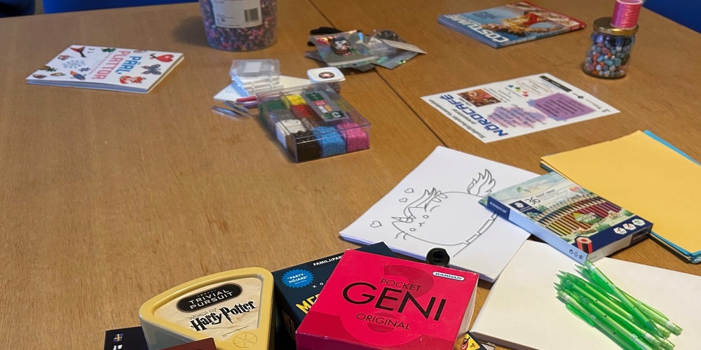 Ett bord med sällskapsspel, kortlekar, papper, pennor och pysselmaterial utspridda.