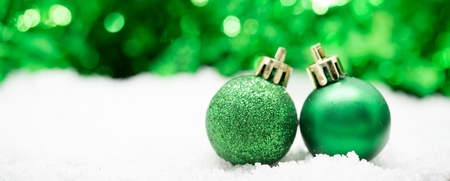 Två gröna julgranskulor står på konstsnö med suddig grön bakgrund.