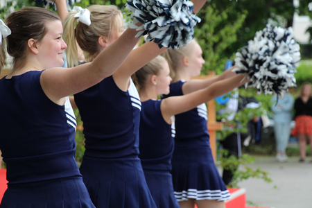 Fyra unga cheerleaders i blå uniformer håller pom-poms och gör en koreograferad rörelse utomhus.