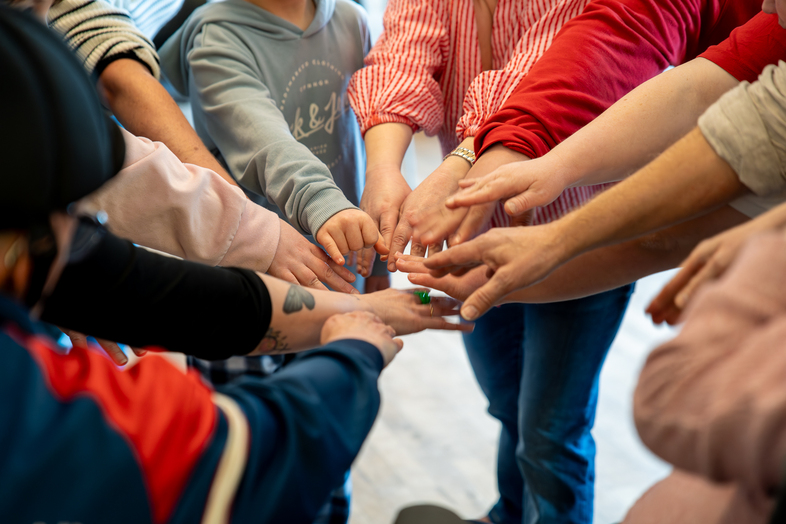 Flera personer står i en cirkel och sträcker in sina händer mot mitten för att röra vid varandra.