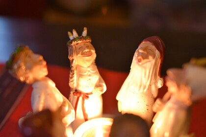 Fyra små figurer i keramik står runt ett ljus, troligen juldekorationer.