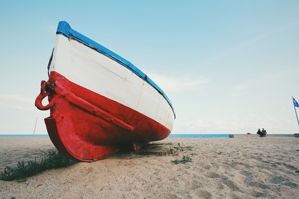 En röd och vit båt står uppdragen på en sandstrand med havet i bakgrunden.