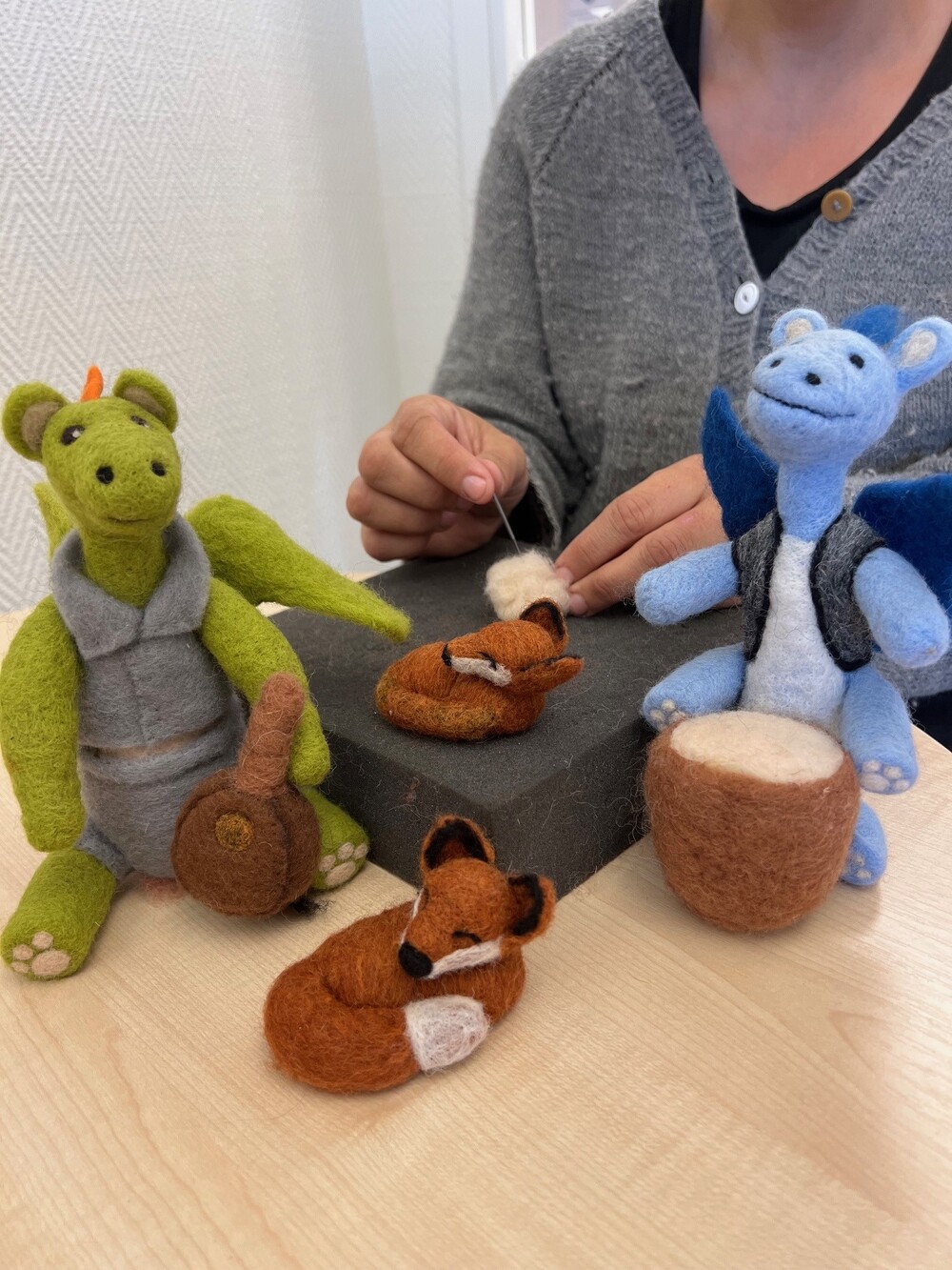 En person nåltovar ullfigurer, inklusive en grön drake, en blå drake och två små rävar, vid ett bord.
