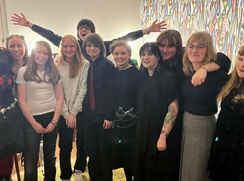 En grupp ungdomar poserar tillsammans inomhus, många klädda i svarta kläder och alternativa stilar.