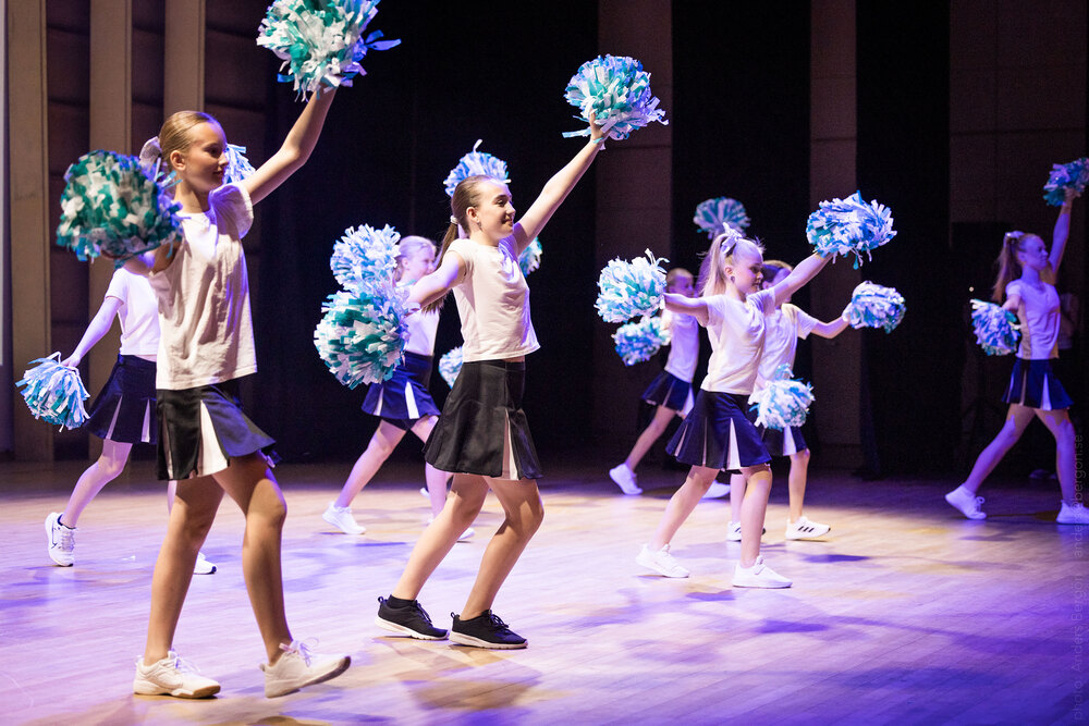 En grupp unga cheerleaders uppträder på en scen med pompoms i händerna.