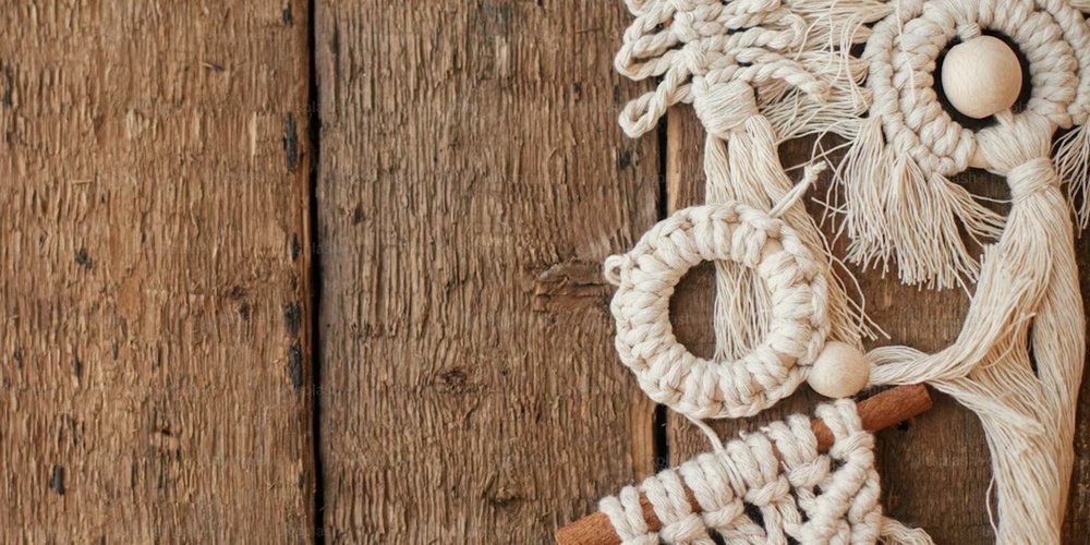 Makramé juldekorationer hänger på en rustik trävägg, inklusive gran, krans och geometriska former.