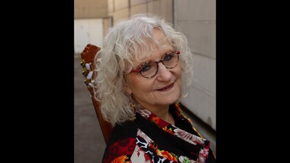 Person med vitt lockigt hår sitter utomhus med en gitarr, ansiktet är suddat.