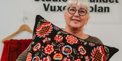 Kvinna med glasögon håller en kudde med färgglatt blommönster framför sig.