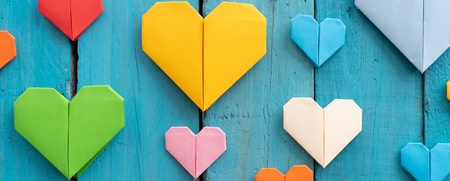 Flera färgglada origamihjärtan i olika storlekar på en blå träbakgrund.