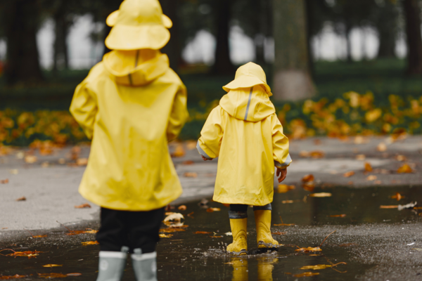 Två barn klädda i gula regnkläder går i vattenpölar.