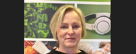 Kvinna med blont hår står framför en affisch med bilder och texten 'Vuxenskolan'.