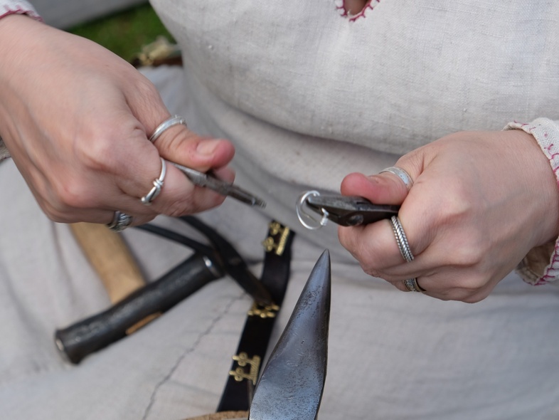 Närbild på händer som arbetar med metallverktyg och ringar, troligen hantverk eller smyckestillverkning.