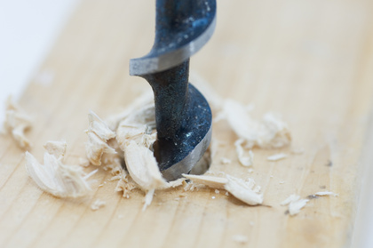 En borr borrar ett hål i en träplanka, träspån syns runt borren.