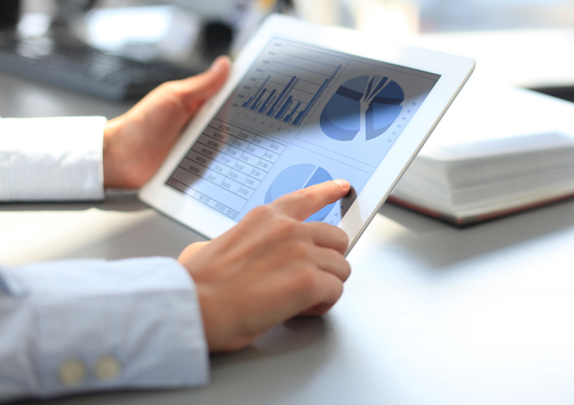 En person använder en surfplatta med diagram och grafer på skärmen vid ett skrivbord.
