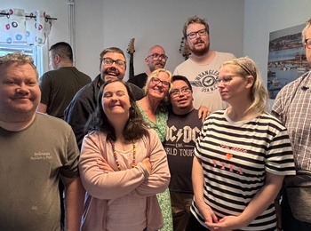 En grupp människor står tillsammans i ett rum med ljusa väggar och fönster, ansikten är suddade.