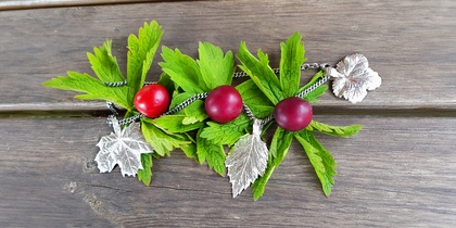 En dekoration med gröna blad, röda bär och silvriga löv ligger på ett träbord.