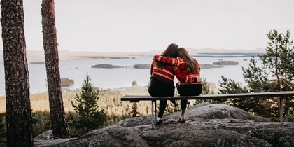Två personer sitter på en bänk med ryggen mot kameran och ser ut över en sjö och skog.