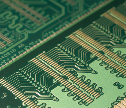 Närbild av ett grönt kretskort med guldiga ledningsbanor och elektroniska mönster.