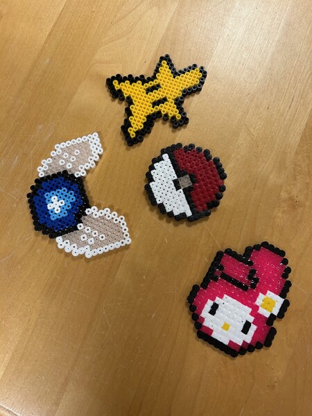 Fyra pärlplattor på ett träbord, föreställande Pikachu, Pokéboll, Navi och My Melody.