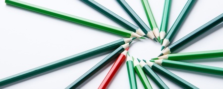 Flera gröna och en röd färgpenna ligger i en cirkel på ett vitt underlag.