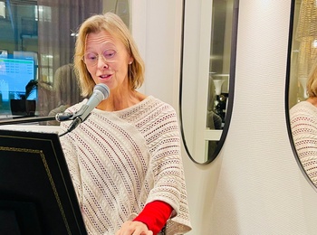 Kvinna spelar keyboard och sjunger i mikrofon, speglas i en rund spegel på väggen.