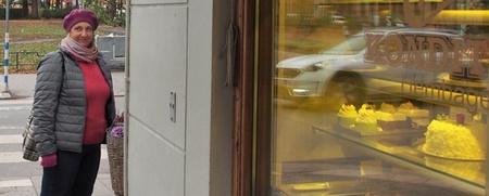 Kvinna i rosa mössa och jacka står utanför ett konditori och tittar in genom skyltfönstret.