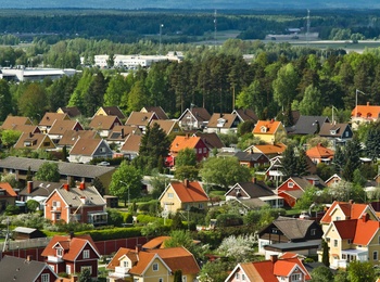 Färgglada villor med röda och gula tak i ett lummigt bostadsområde, omgivna av skog och berg i bakgrunden.