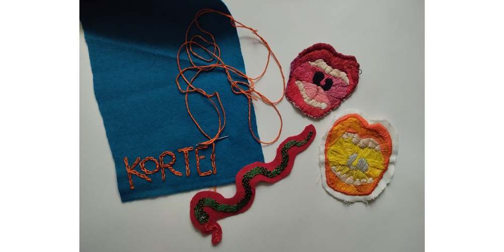 Färgglada broderier på tyg, inklusive en orm, två cirkulära former och ordet 'KORTEI' på blå filt.