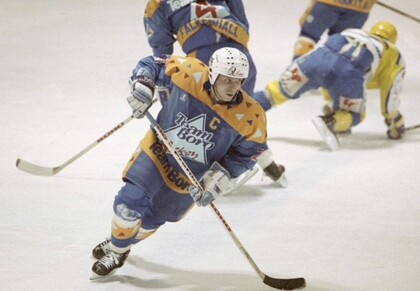Ishockeyspelare i blått och gult lag dribblar med pucken på isen under en match.
