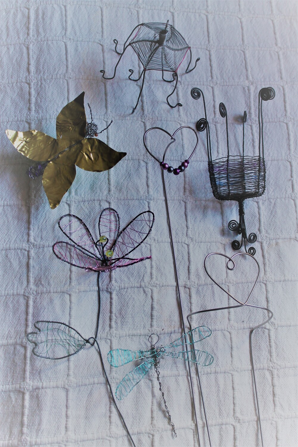 Konstnärliga figurer av metalltråd och papper föreställande blommor, hjärtan, en fjäril och en trollslända mot vit bakgrund.