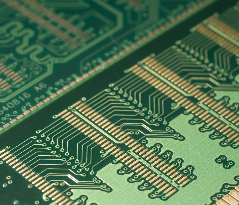 Närbild av ett grönt kretskort med guldiga ledningsbanor och elektroniska mönster.
