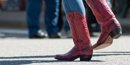Person i blå jeans och röda cowboyboots dansar utomhus på asfalt.